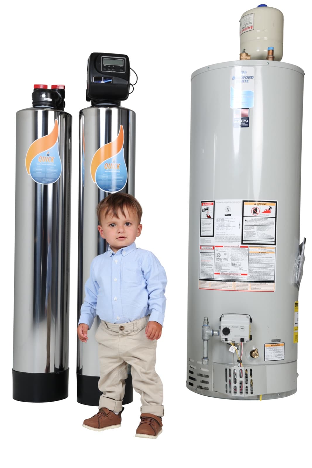 A young boy standing beside two Quick whole house filtration tanks and a water heater