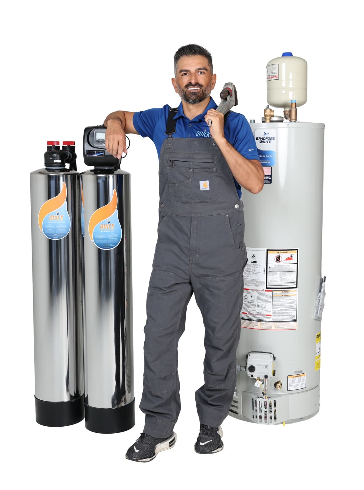 A Quick Water Heater technician in work overalls beside a water heater and filtration tanks